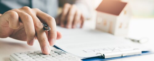 person using calculator next to notepad and model house