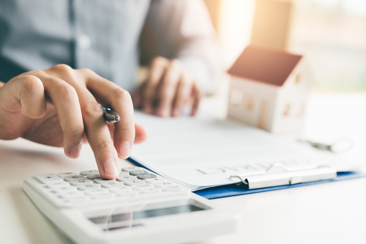 person using calculator next to notepad and model house